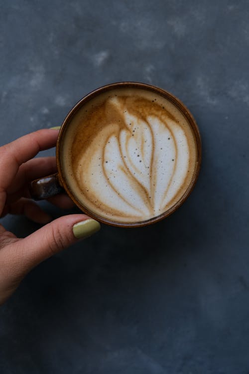 A hand holding a cup of coffee with a latte art design