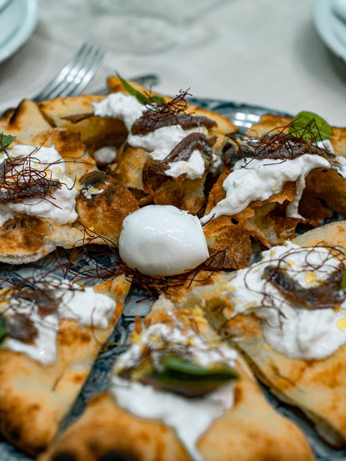 Free Close-up of a gourmet pizza topped with creamy burrata, anchovies, and fresh garnish. Stock Photo
