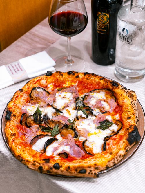 Free Appetizing pizza with mozzarella and ham served with red wine in a cozy restaurant setting. Stock Photo