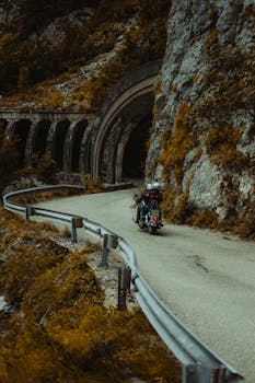 Motorcyclist explores a scenic mountain road with a rugged tunnel entrance.