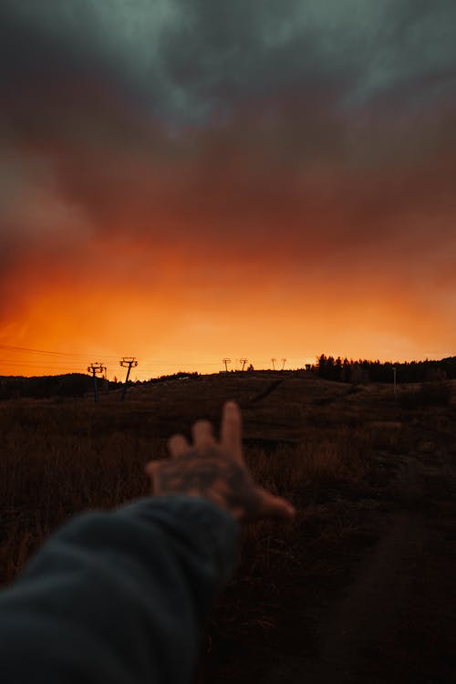A person's hand reaching out to the sky at sunset