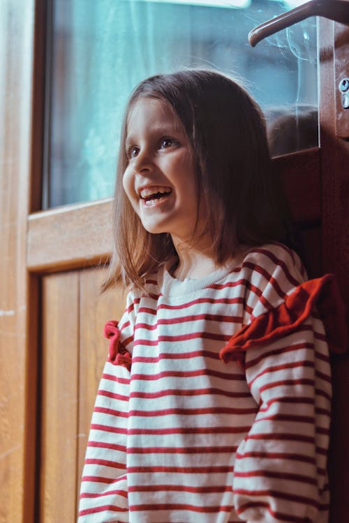 Small Girl in a Striped Blouse Smiling and Leaning Against a Door