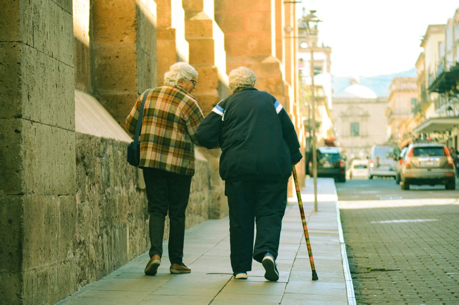 Una pareja de ancianos camina por una calle iluminada por el sol en Morelia, México, abrazando la compañía.