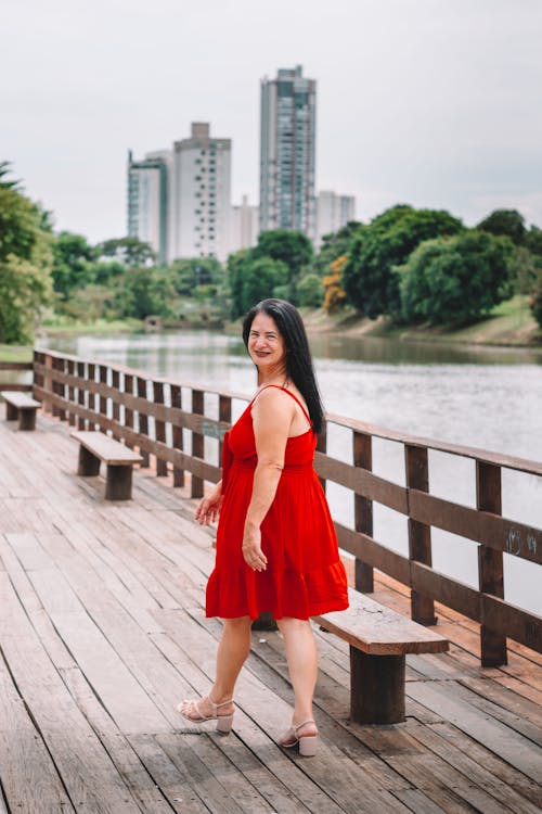A woman in a red dress is standing on a wooden bridge