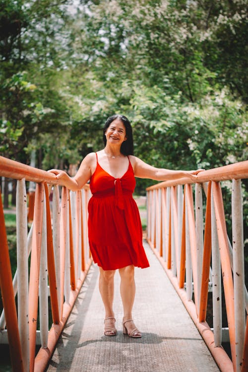 A woman in a red dress stands on a bridge