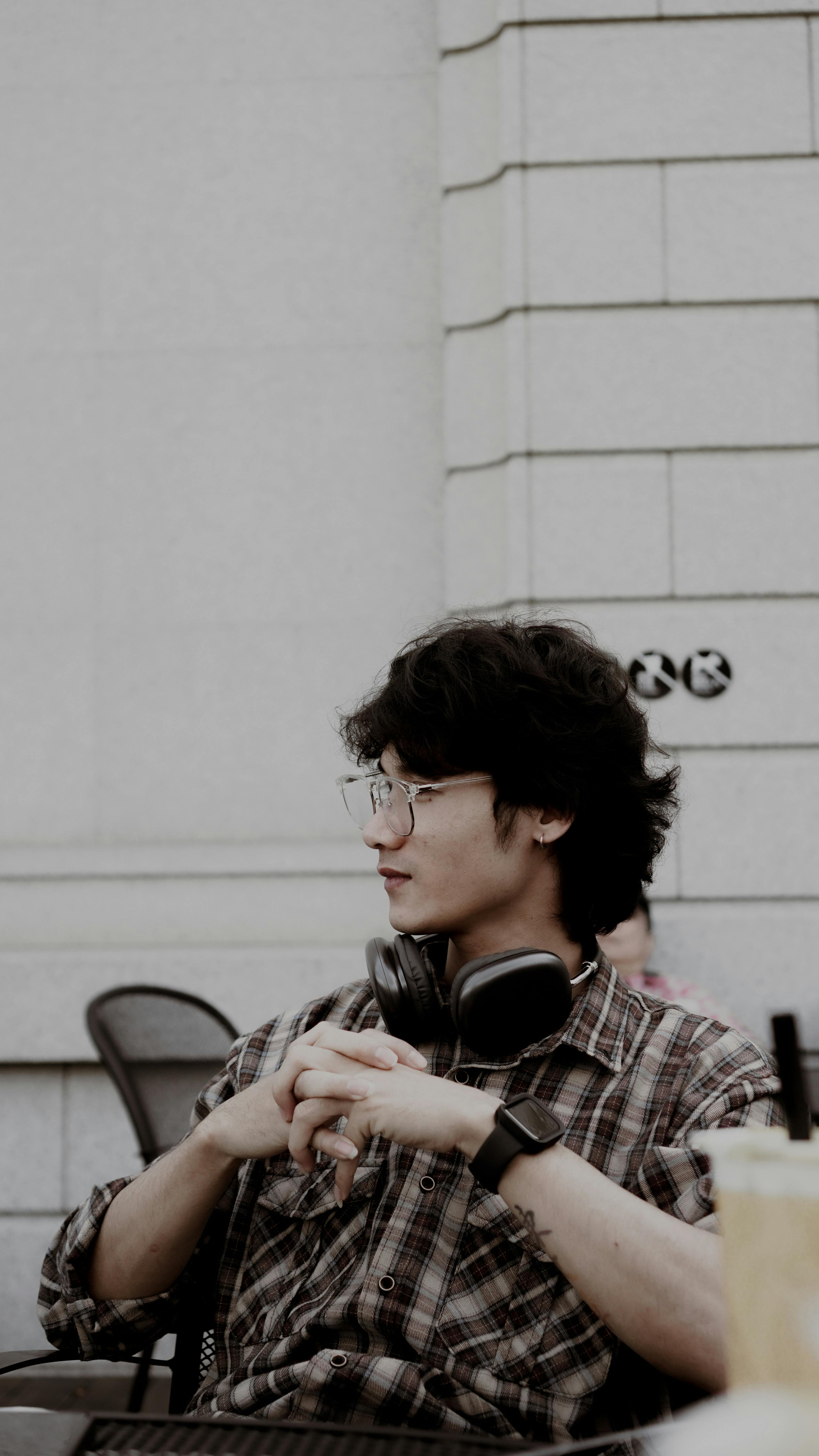 Profile portrait of a young man with headphones and glasses sitting in a modern outdoor setting.