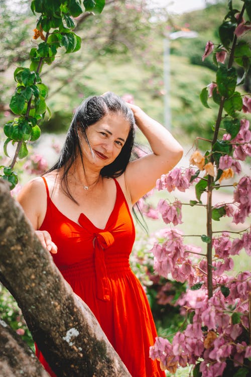 A woman in a red dress posing near a tree
