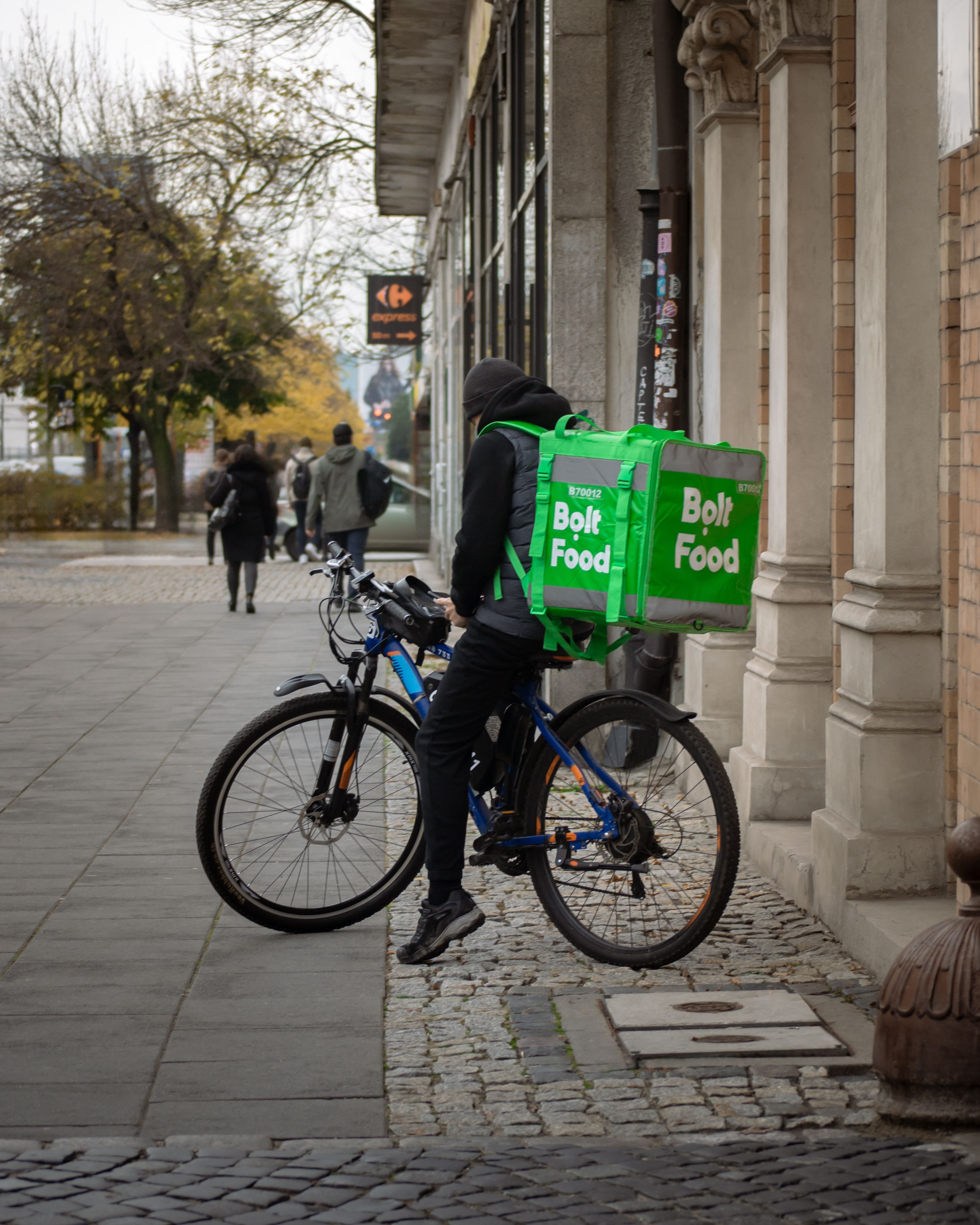 A cyclist delivers food on a city street with a Bolt Food ba