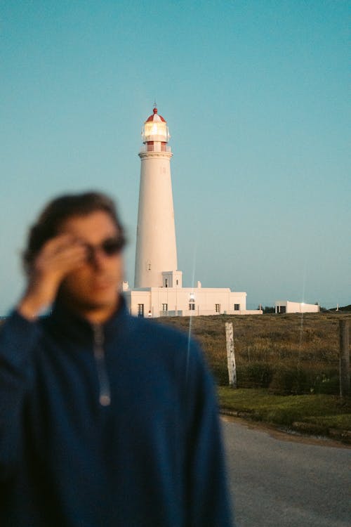 Walking person taking off sunglasses and lighthouse in the background