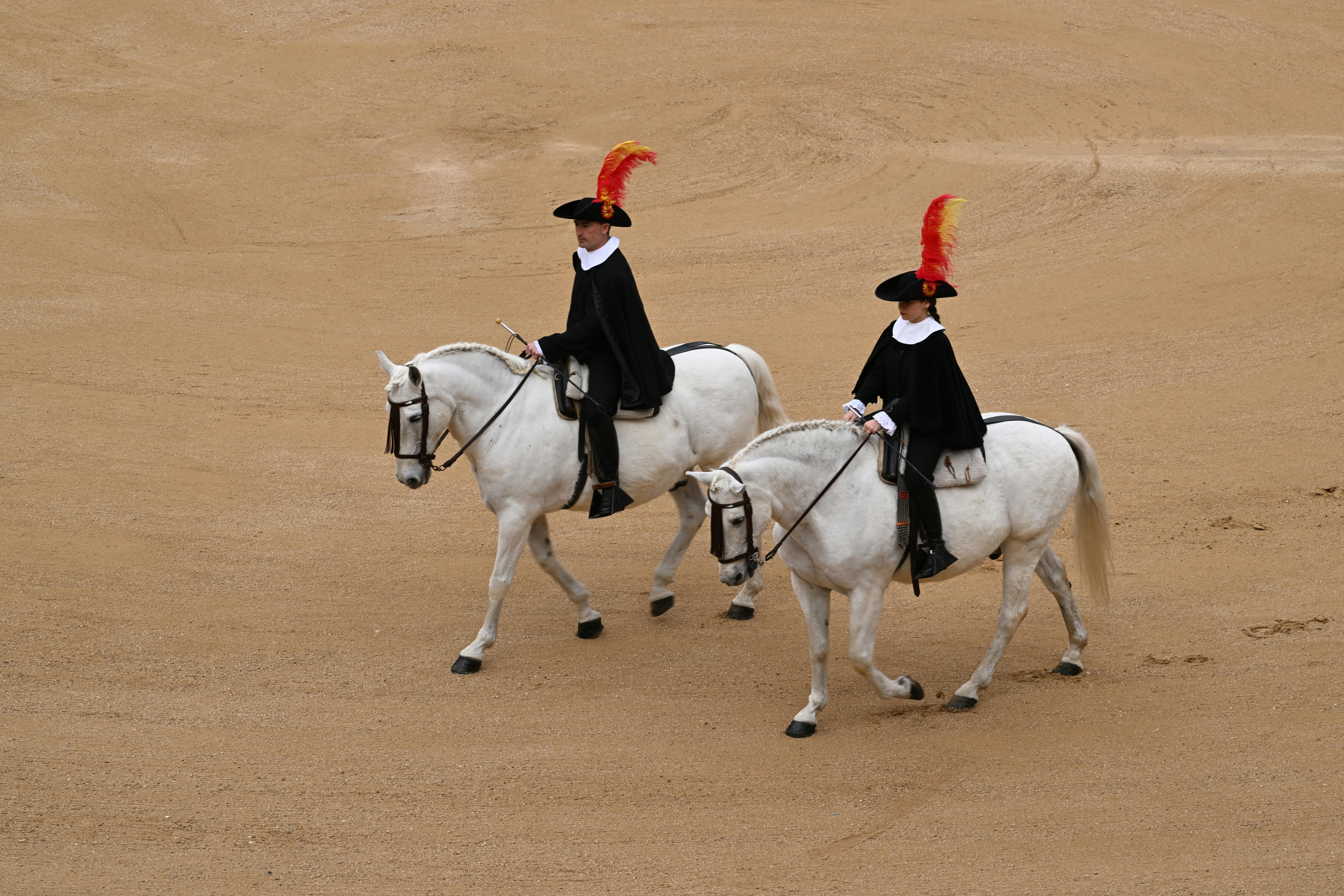 Two equestrians on white horses in traditional attire at Madrid arena.
