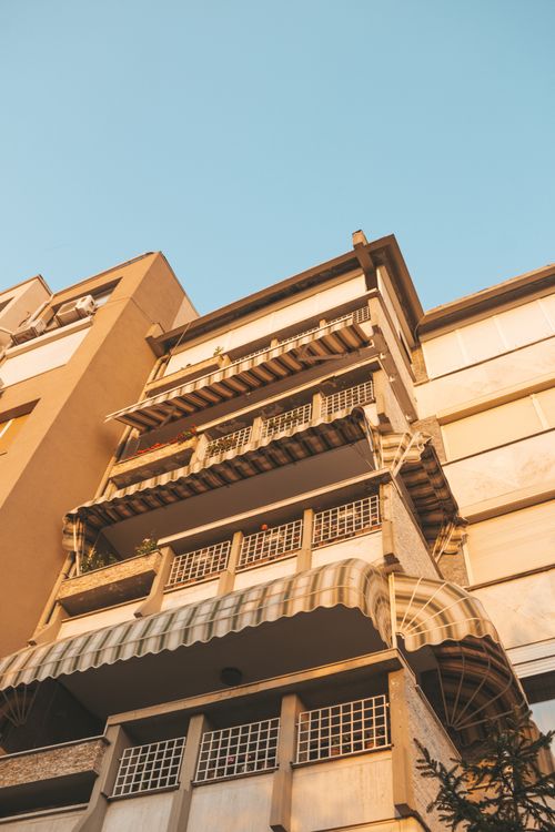 Free From below exterior of residential building of beige color with balconies decorated with cozy tents against cloudless blue sky Stock Photo