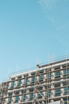 From below exterior of extensive scaffolding for workers to build new building block against cloudless blue sky work in progress
