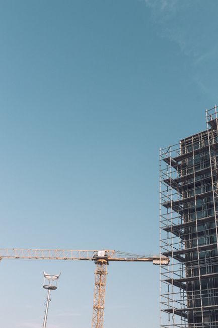 Low angle crane near tall skyscraper with scaffolding against blue cloudless sky