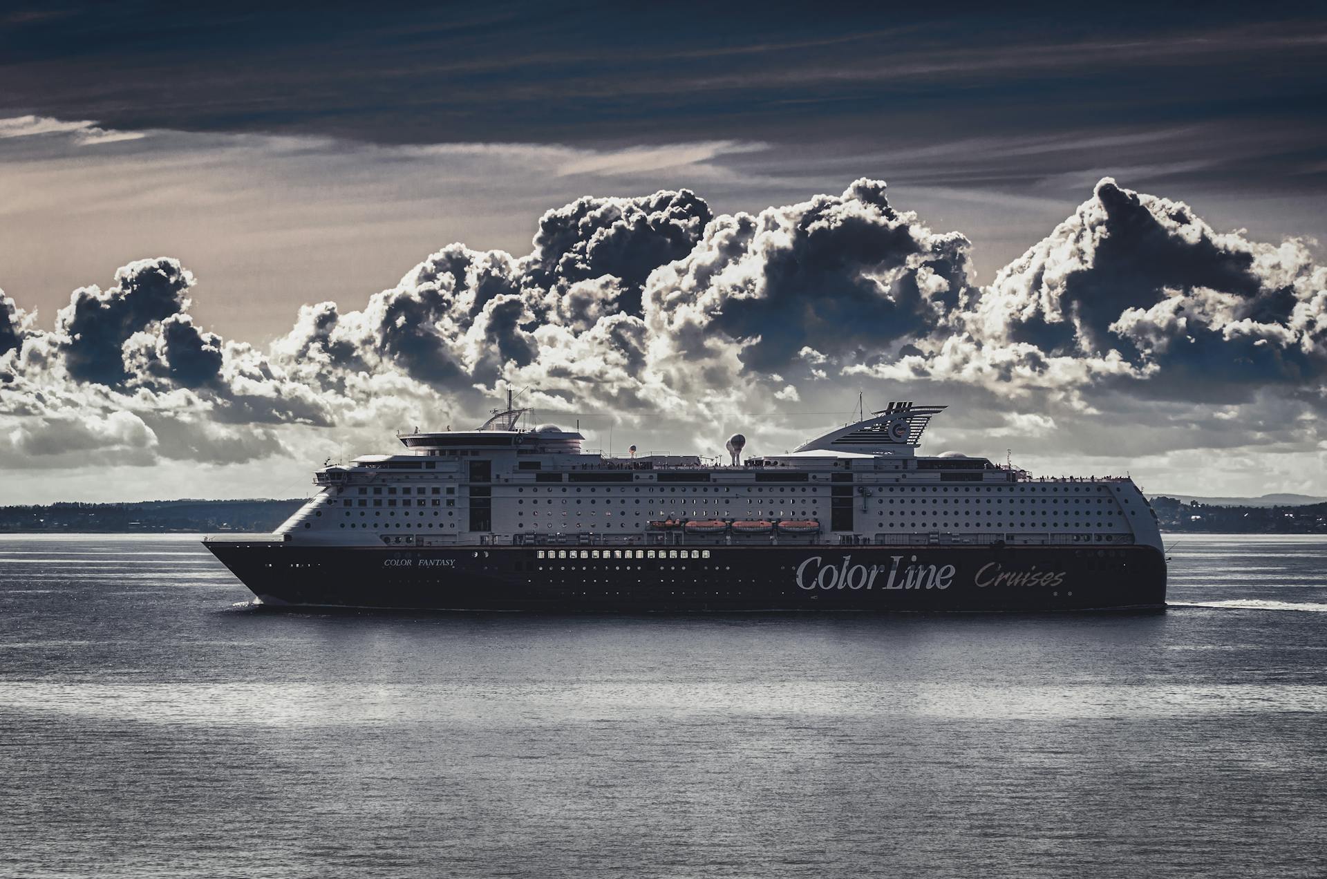 A stunning cruise ship navigates the calm ocean beneath striking, billowing clouds.