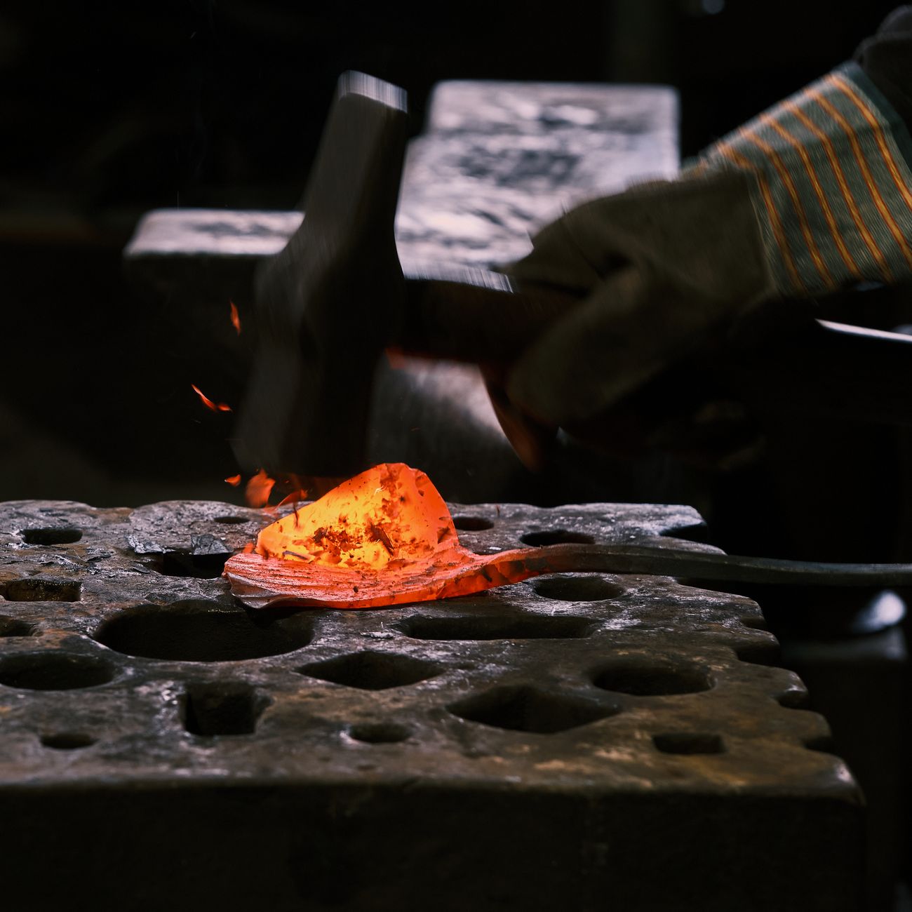 A skilled blacksmith forging red-hot metal on an anvil in an industrial workshop.