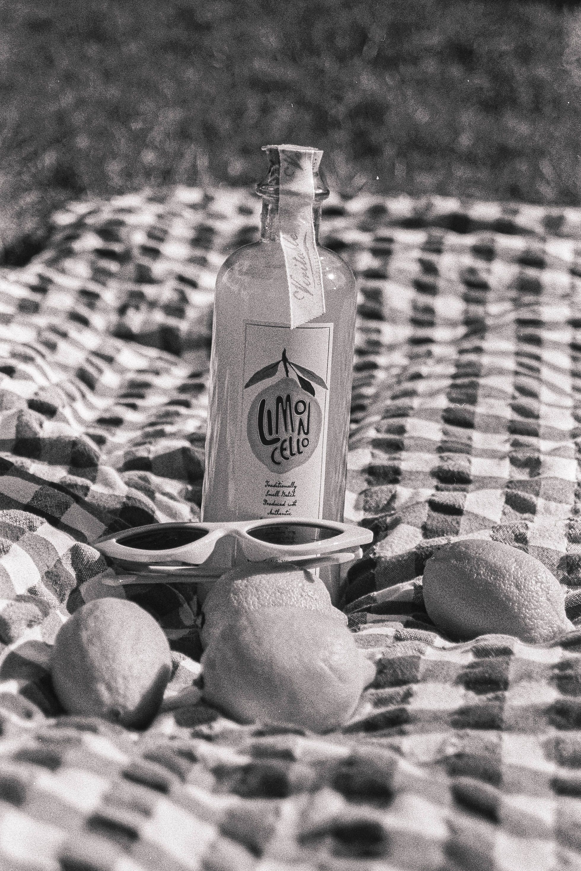 A stylish black and white photo of a limoncello bottle on a picnic blanket with sunglasses and lemons.