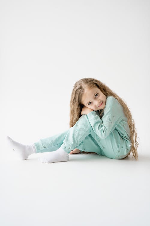 A little girl sitting on the floor wearing a green pajama