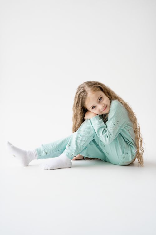 Free Charming young girl with long blonde hair sitting in pajamas on a white background, smiling and relaxed. Stock Photo