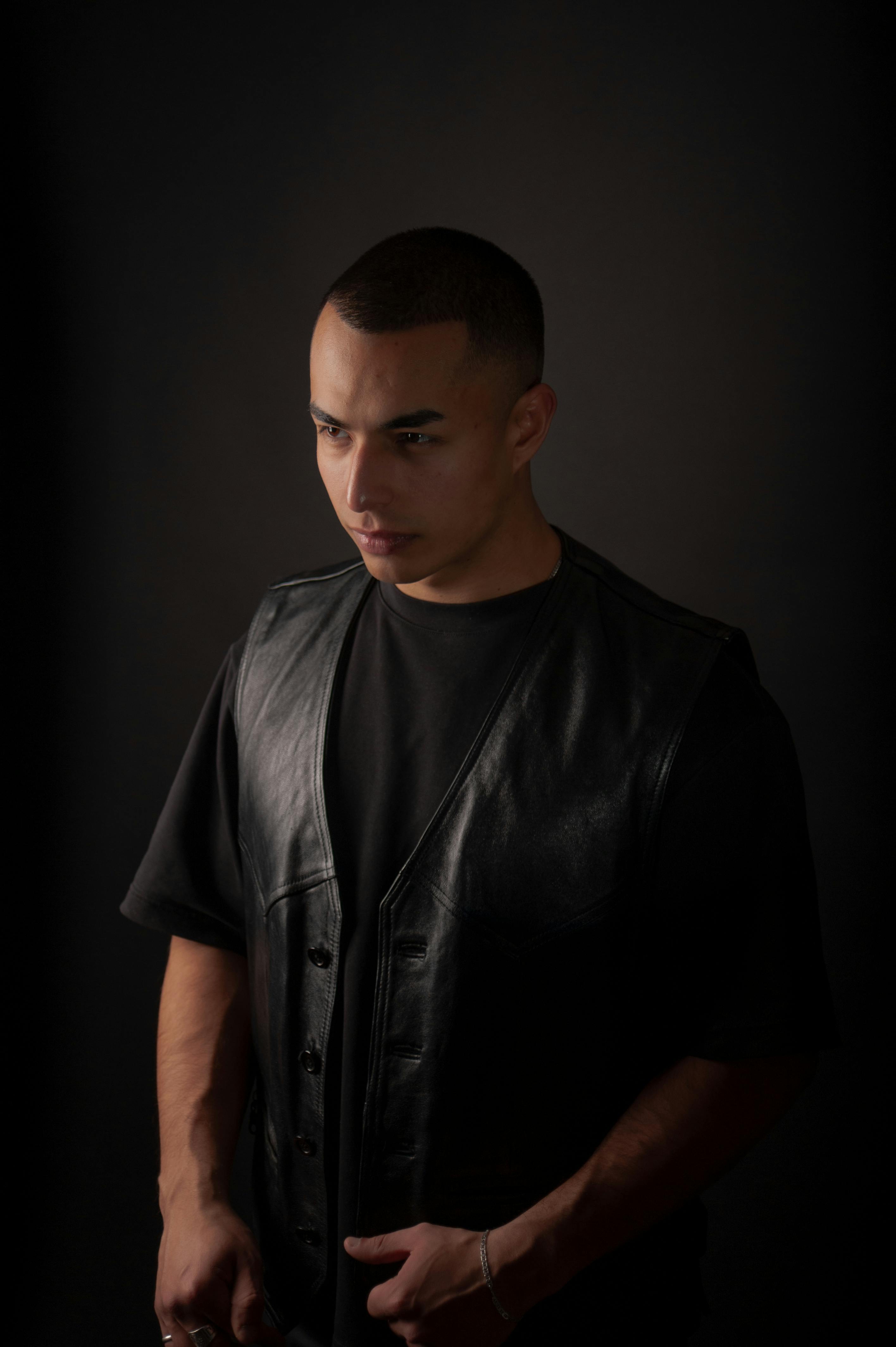 Free Portrait of a fashionable man in a studio wearing a leather vest, creating a moody atmosphere. Stock Photo