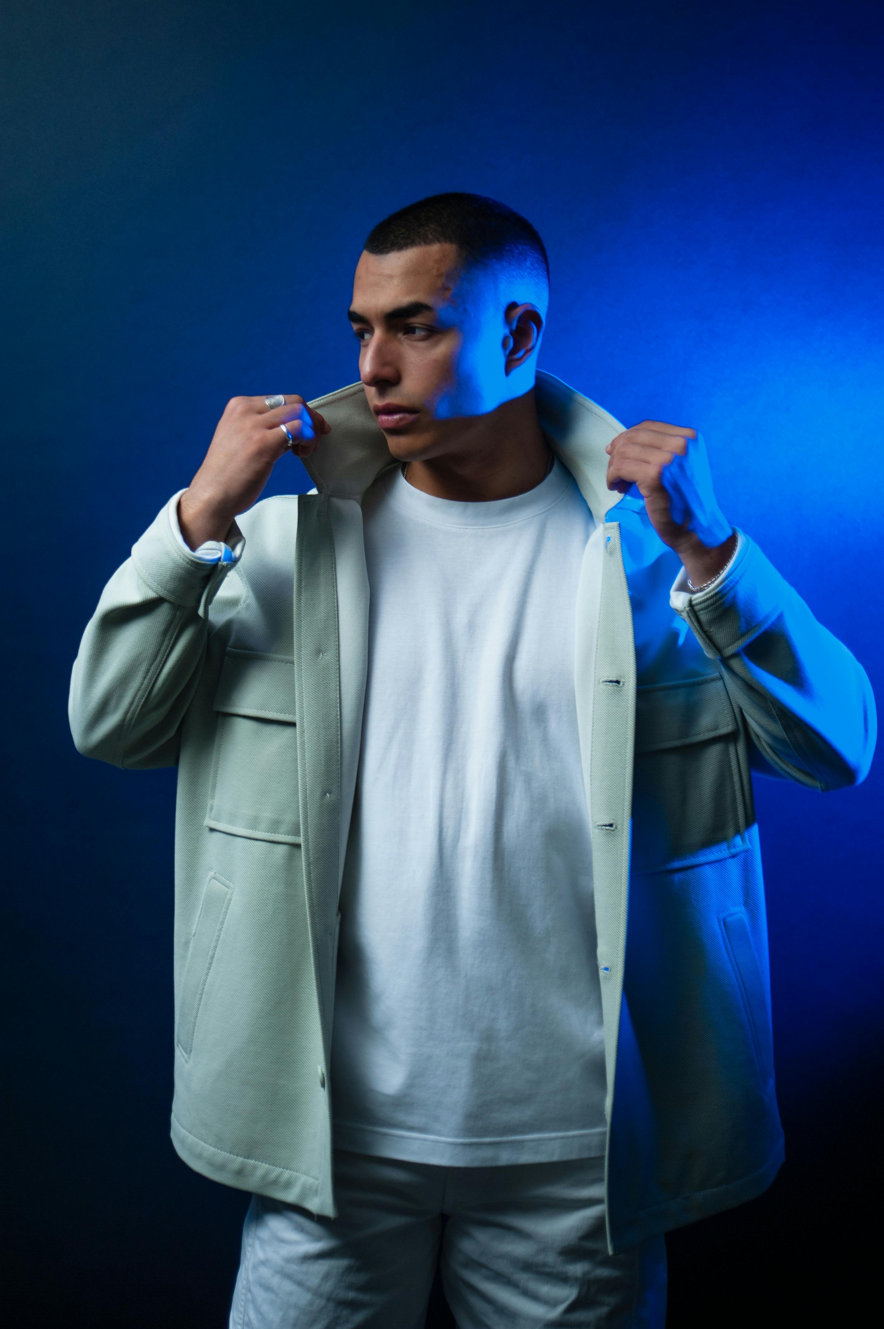 Free Stylish portrait of a man in a white jacket under dramatic blue lighting, showcasing modern fashion. Stock Photo