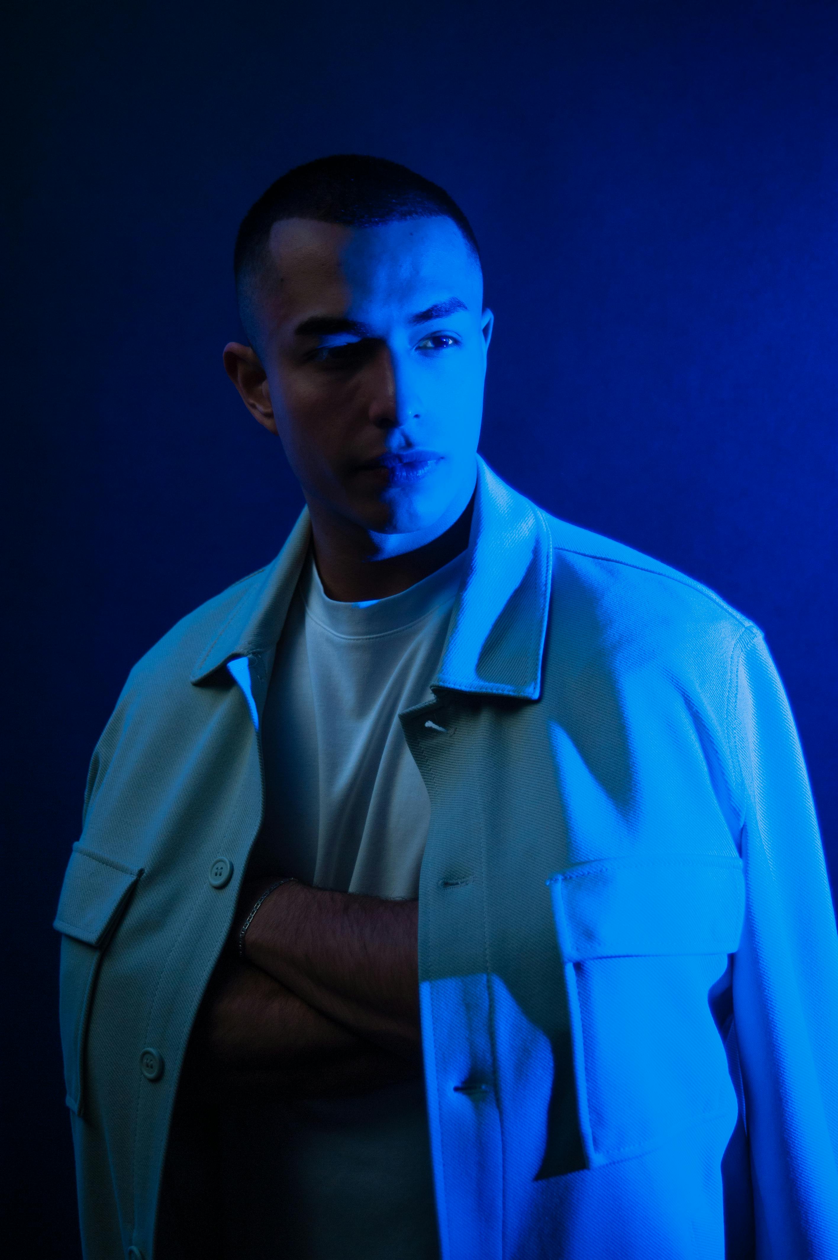 Free Portrait of a man in a blue-lit studio, wearing a white jacket with arms crossed. Stock Photo