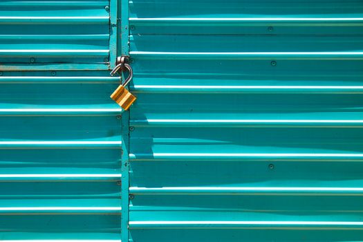 Close-up of a turquoise metal door with a golden padlock, emphasizing security.