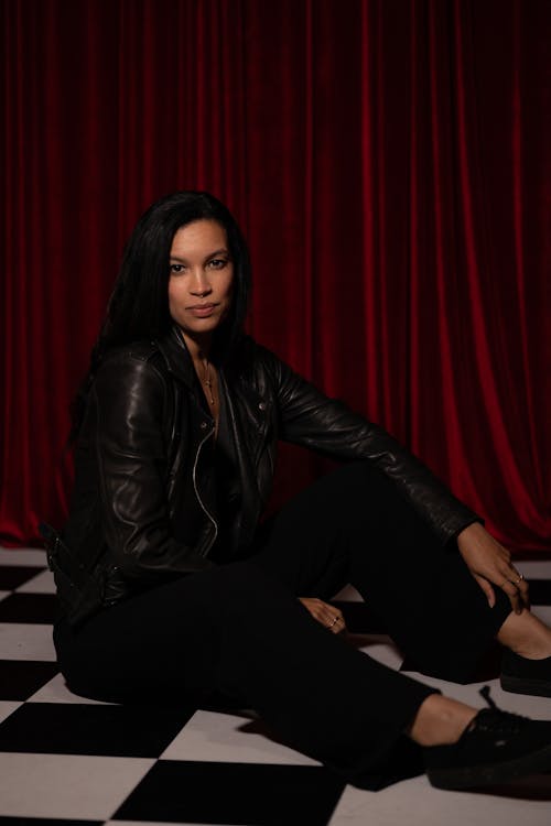 A woman in black pants and jacket sitting on a checkered floor