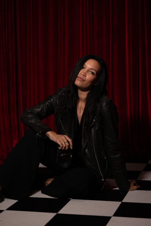 A woman in a leather jacket sitting on a checkered floor
