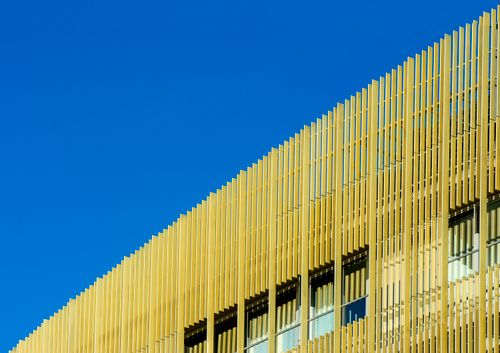 Free A modern building facade with unique vertical elements against a clear blue sky. Stock Photo
