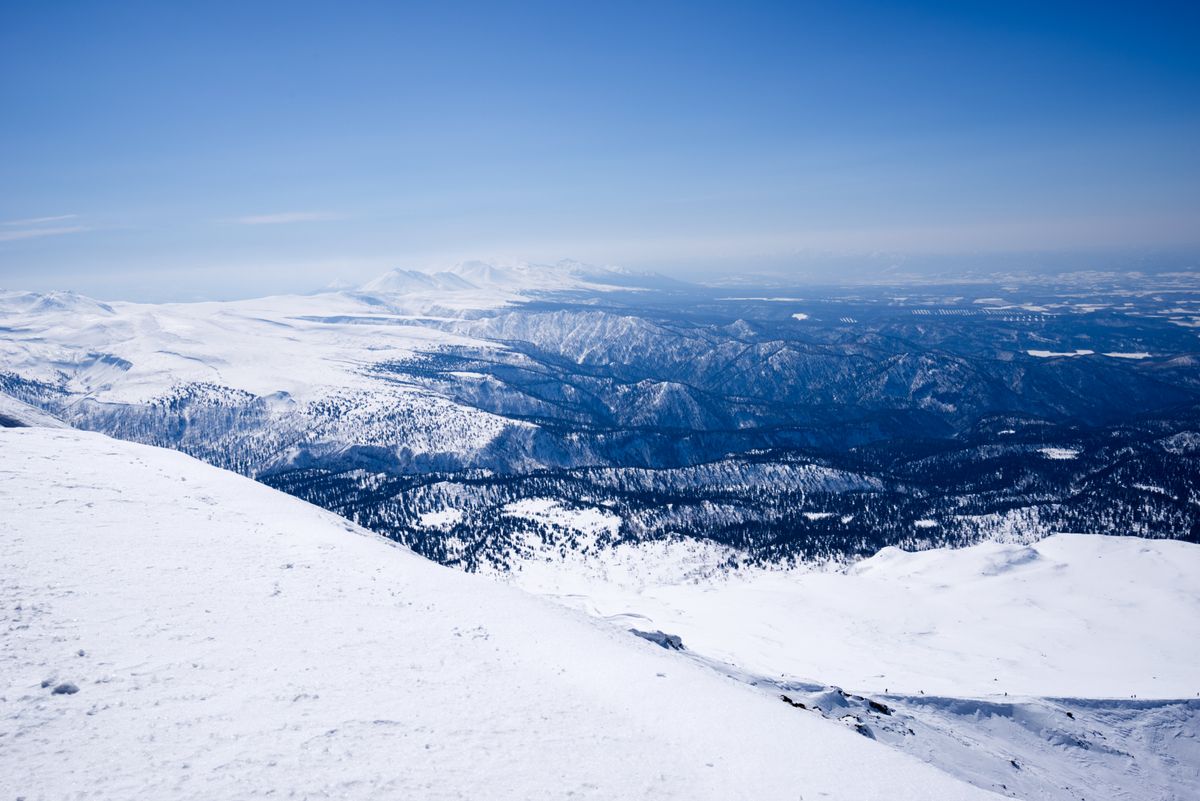 A sweeping aerial view of snow-covered mountains and forested hills stretching to the horizon in Hokkaido