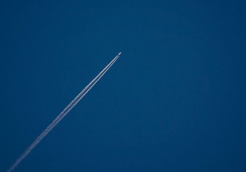 Free High-altitude airplane leaving contrails across a clear blue sky, symbolizing travel. Stock Photo