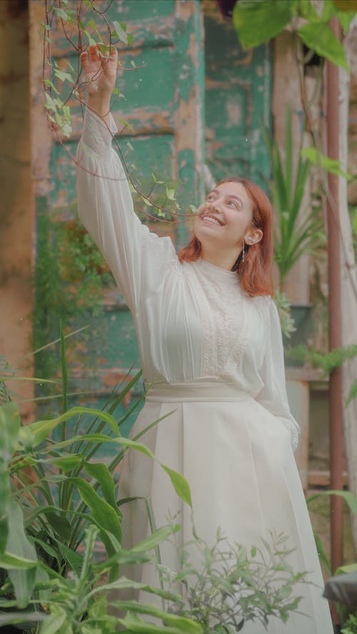 A woman in a white dress is holding up a plant