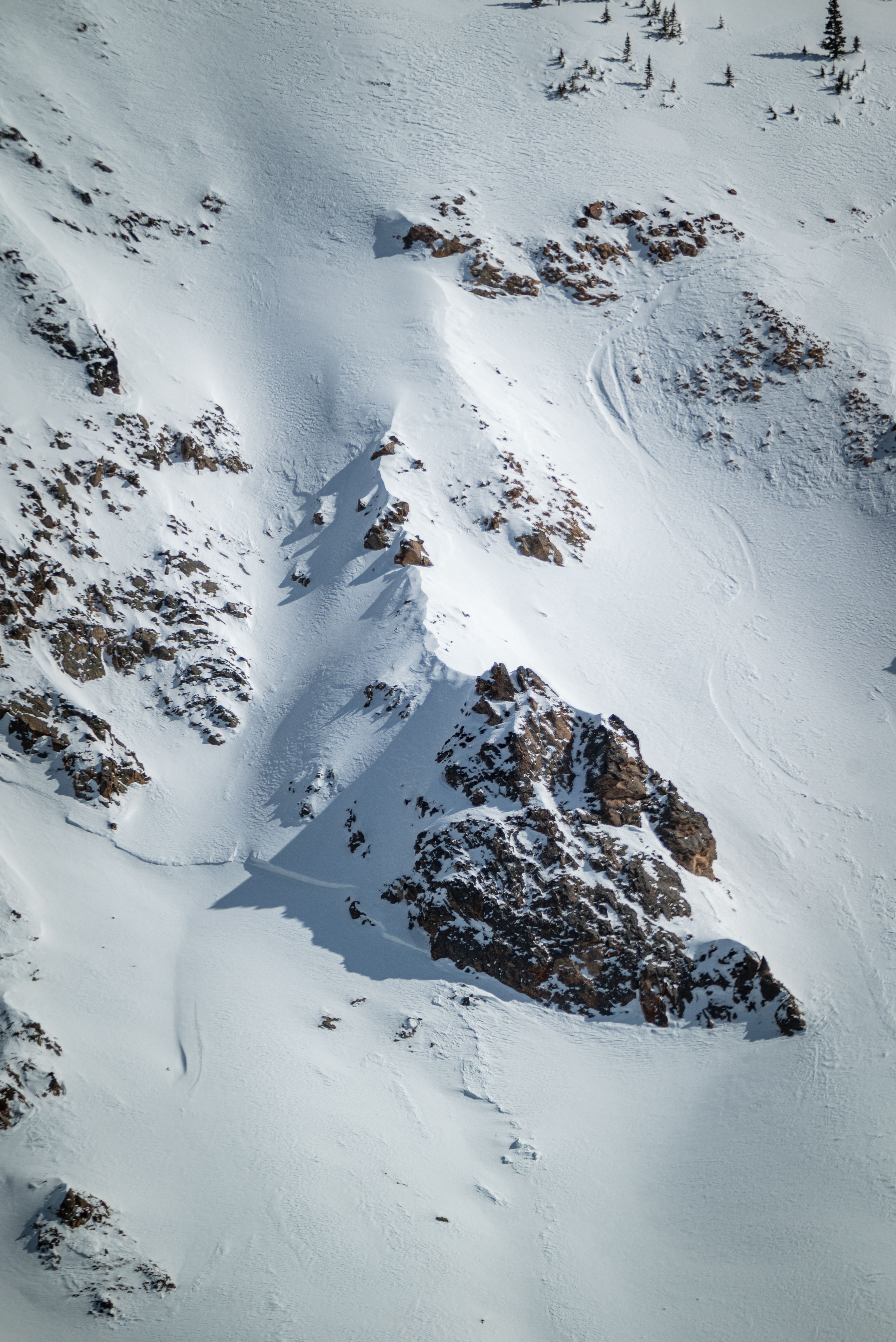 Aerial view of a snowy mountain slope with rugged rock formations, evoking winter's natural beauty.