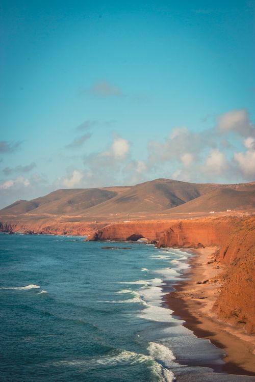 Free Scenic aerial view of a rugged coastline with red cliffs and a blue sea under a clear sky. Stock Photo