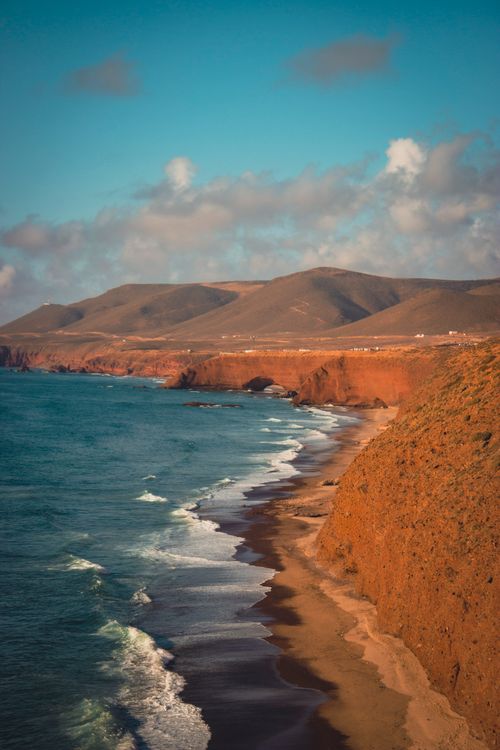 Free A stunning aerial view of a coastline with rugged cliffs and clear blue sea under a bright sky. Stock Photo