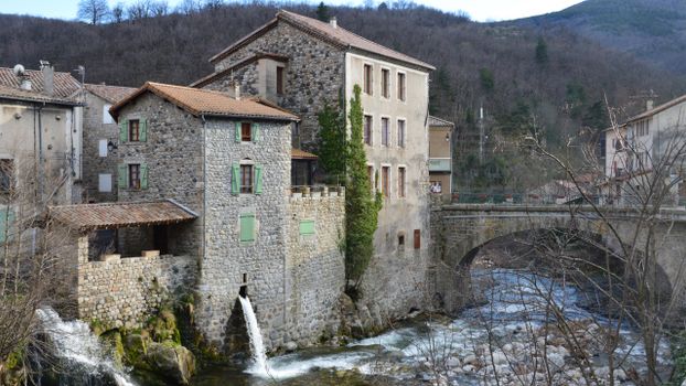 Charming stone houses beside a flowing river in Burzet, showcasing picturesque French village architecture.
