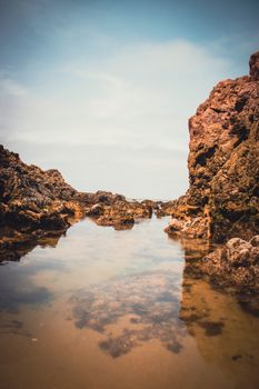 Tranquil coastal rock formation with a reflective tide pool under a clear sky, showcasing natural erosion.. pexels, tranquil,