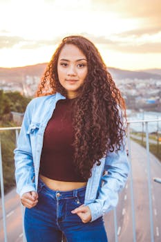 一位穿着牛仔夹克、留着卷发的时尚年轻女子在日落时分的户外摆姿势
