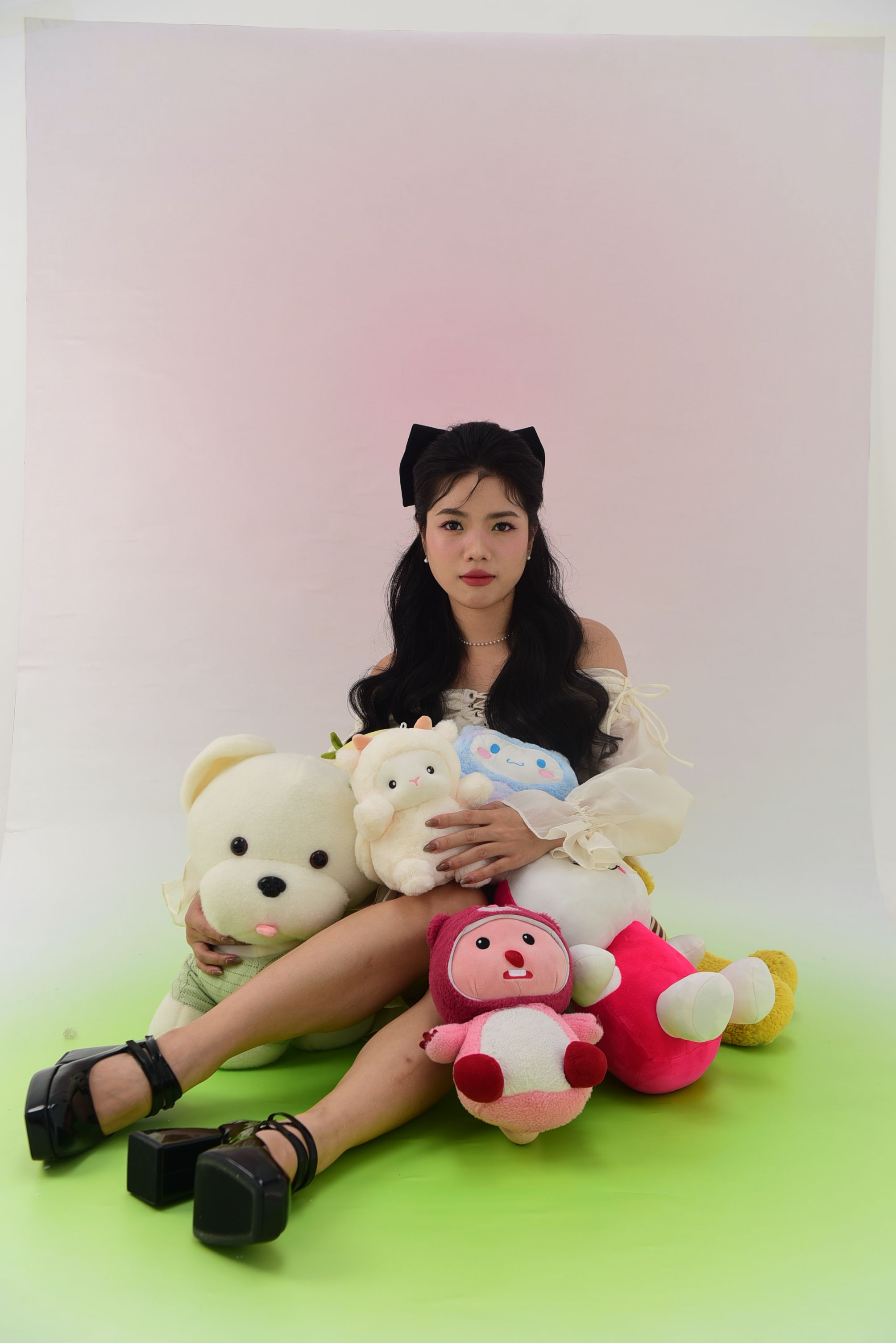 Portrait of a young woman sitting with plush toys in a studio setting, showcasing playful fashion and accessories.