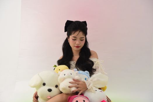 Charming portrait of an Asian woman holding various plush toys in a bright studio setting.