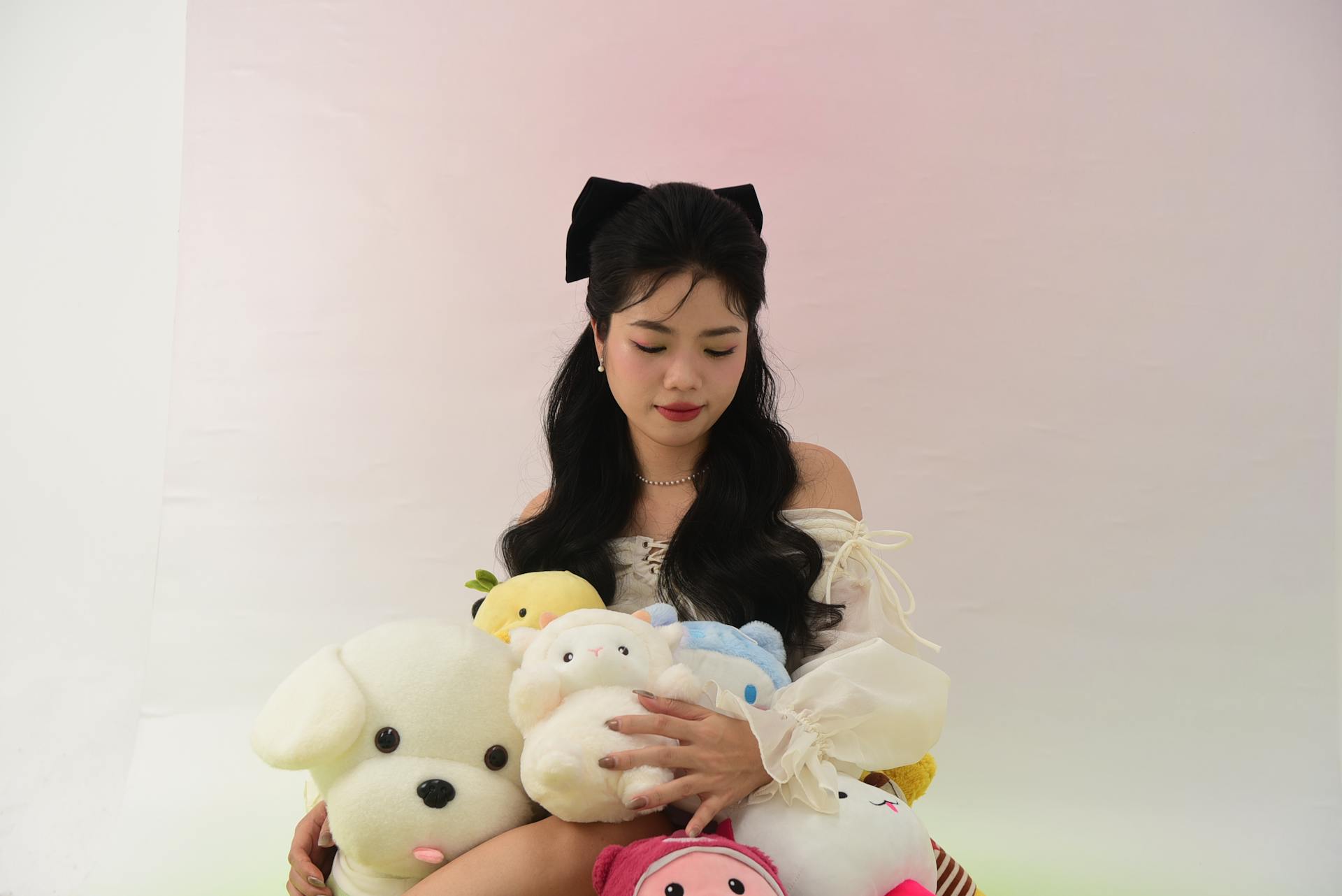 Charming portrait of an Asian woman holding various plush toys in a bright studio setting.