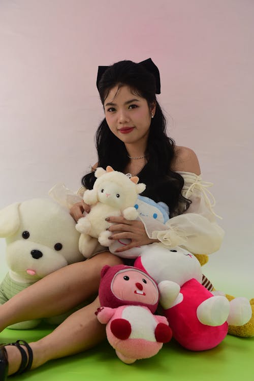A woman sitting on the ground holding a bunch of stuffed animals