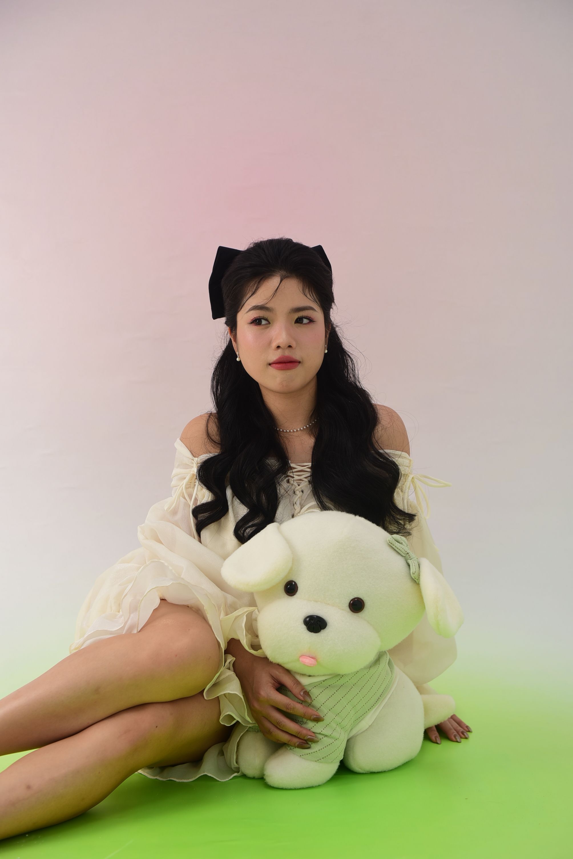 Asian woman in stylish attire sitting with a plush dog toy in a studio setting.