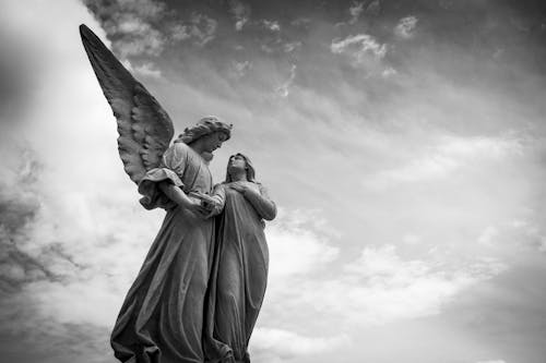Фотография статуи ангела под облачным небом в оттенках серого