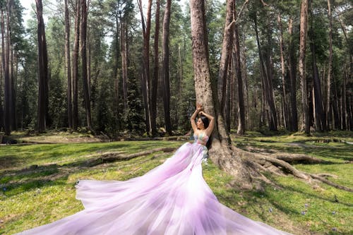 A woman in a long purple dress is standing in the woods
