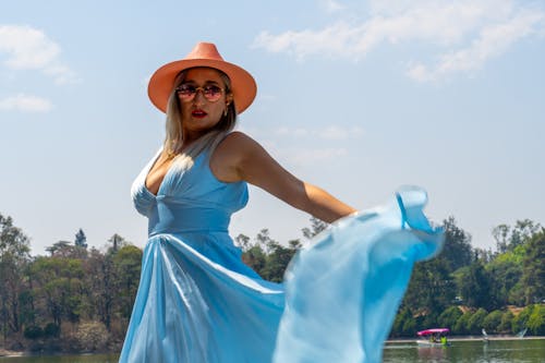 A woman in a blue dress and hat is posing on the water