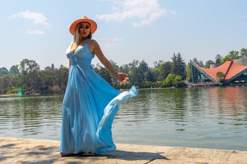 A woman in a blue dress and hat is standing by the water