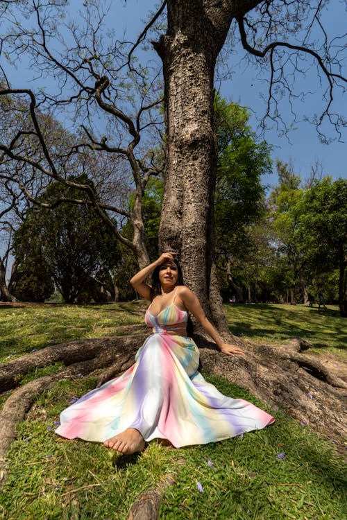 A woman in a rainbow colored dress sitting on the ground