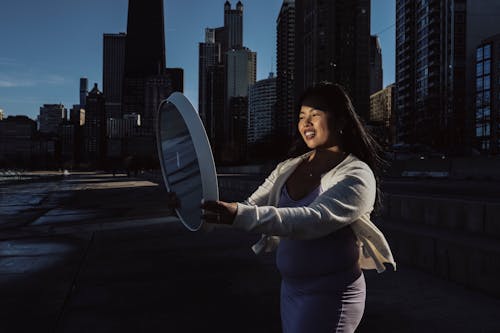 A pregnant woman holding a white object in front of a city skyline