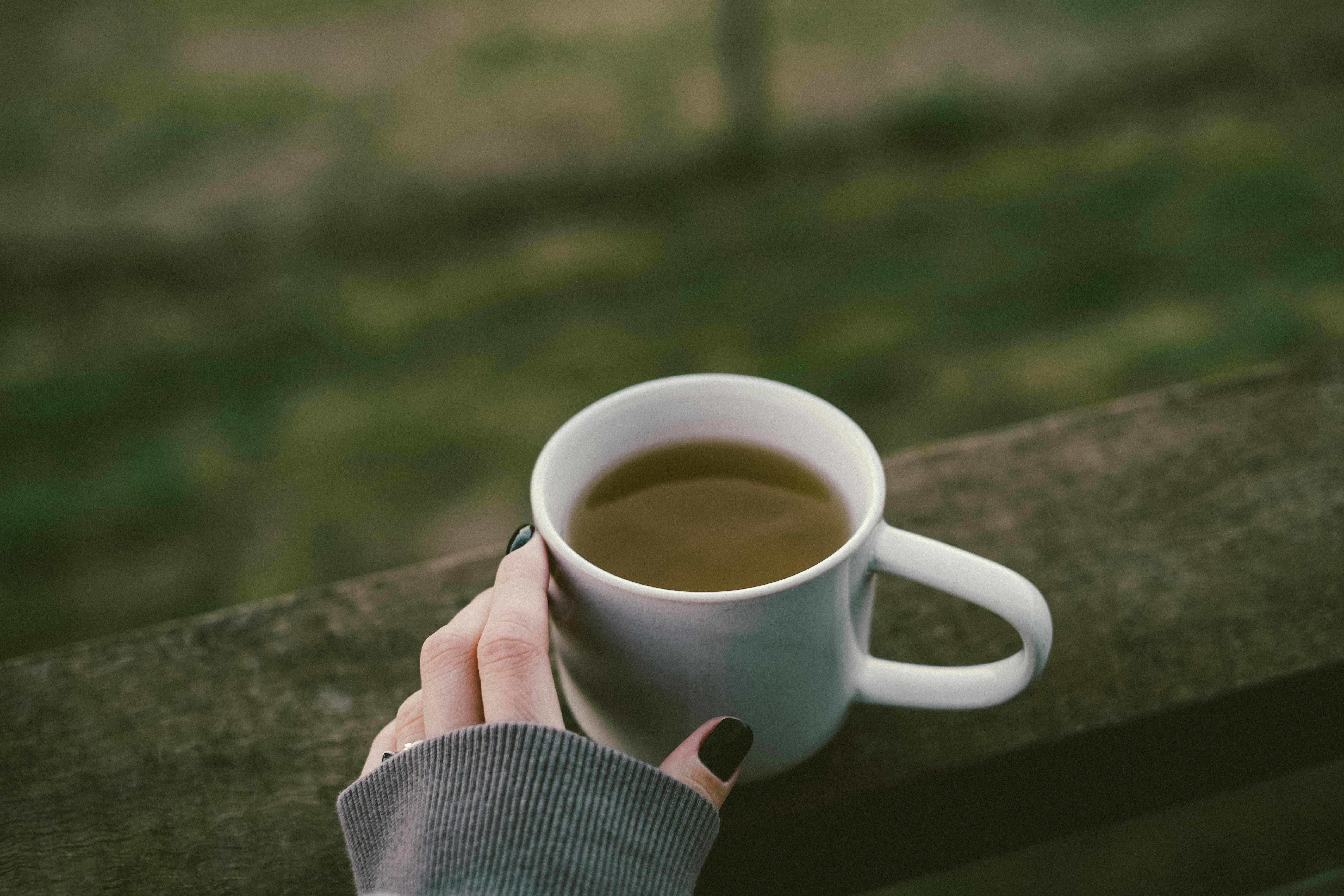Closeup of a hand holding a mug of tea or coffee outdoors, capturing a serene morning moment.